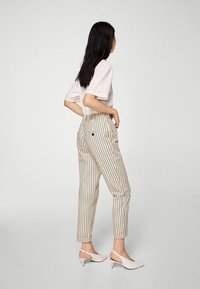 Pantaloni a righe beige chiaro con vita alta, dotati di due tasche posteriori, abbinati a tacchi a schiaccio bianchi e una maglietta dal taglio largo.