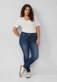 Blauwe denim jeans met een slim fit en vijf zakken, gecombineerd met een witte V-hals T-shirt met korte mouwen en beige sneakers.