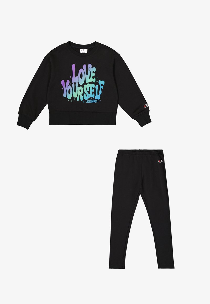 Sudadera corta negra con el gráfico "Ámate a ti mismo" en colores pastel; combinada con leggings negros. Ambos presentan detalles del logo de Champion.