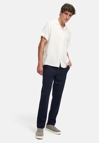 Camisa blanca de manga corta y botones en tela texturizada, combinada con pantalones navy y zapatos grises con cordones. Diseño simple y corte relajado.