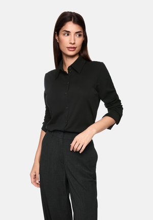Black button-up shirt with a collar, long sleeves, and a smooth texture, paired with dark gray tailored trousers.