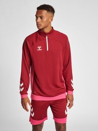 Röd sportig långärmad tröja med halvmatch, med mesh-detaljer och rosa accenter. Kombinerad med matchande röda shorts och vit varumärkeslogotyp.
