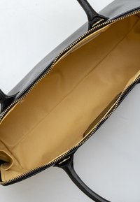 Borsa a mano in pelle nera con una texture liscia, cerniera dorata e interno beige. Presenta manici doppi e un ampio scomparto principale.