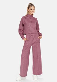 Paarse cropped sweatshirt met halve rits, textuurpatroon en lange mouwen, gecombineerd met losse, bijpassende wijde broek. Witte sneakers zichtbaar.
