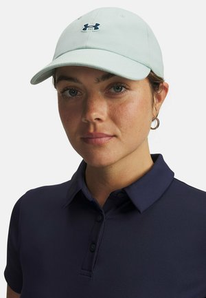 Lichtgroene pet met een gebogen klep en een marineblauw Under Armour-logo. Draagt bij een marineblauw poloshirt met een kraag en knopen.