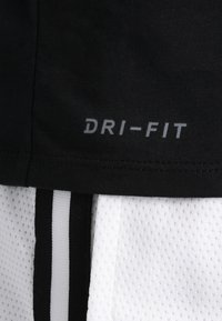 Schwarzer Stoff mit dem Text "DRI-FIT" über einem weißen Netzstoff, der mit schwarz-weißen vertikalen Streifen versehen ist.