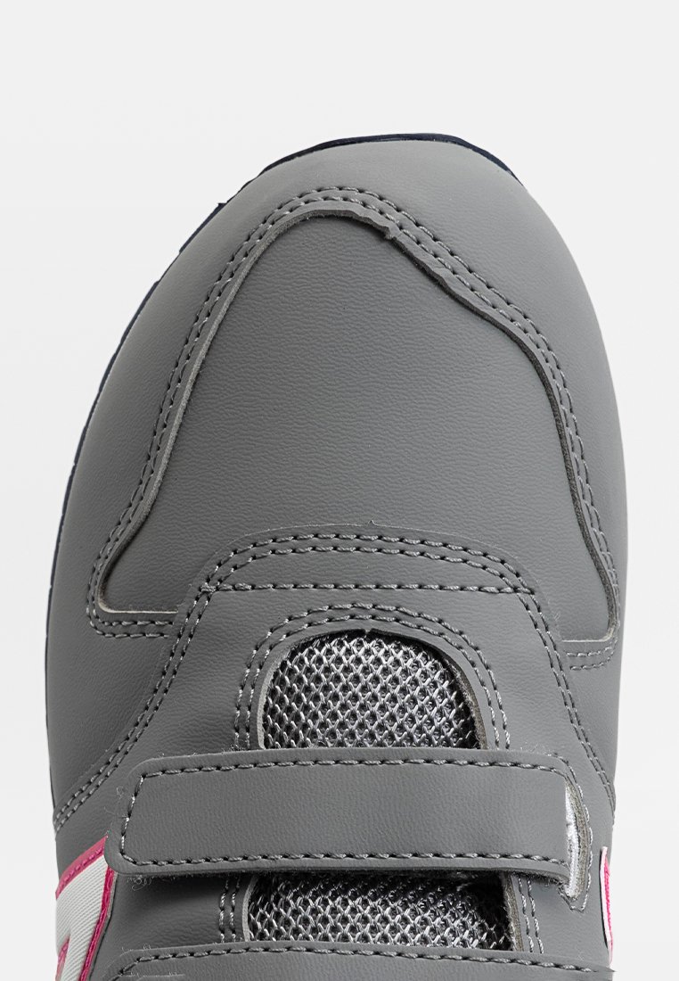 Zapatilla deportiva gris con parte superior de cuero suave, secciones de malla para transpirabilidad y dos correas de Velcro para el cierre. Incluye detalle de acento rosa.
