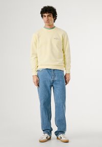Geel katoenen sweatshirt met ribgebreide manchetten en halslijn, gedragen over een lichtblauw t-shirt, gecombineerd met lichtblauwe rechte spijkerbroek.