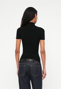 Μαύρο πλεκτό τοπ με ριγέ υφή, ψηλό γιακά και κοντά μανίκια, σε συνδυασμό με σκουρόχρωμο παντελόνι τζιν και μαύρη δερμάτινη ζώνη.