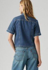 Giacca in denim corta a maniche corte di colore blu scuro, con colletto classico, vestibilità strutturata e dettagli di cucitura a vista.
