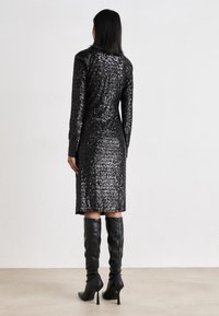 Vestido preto de lantejoulas com mangas longas, corte até ao joelho, fendas laterais, combinado com botas altas de couro pretas, textura suave e superfície refletora.