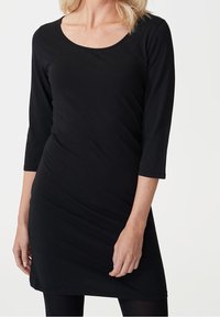 Černé šaty s dlouhým rukávem, s kulatým výstřihem, střih přiléhající na tělo a jemně hladká textura. Délka až do poloviny stehen. Jednoduchý design bez vzorů.