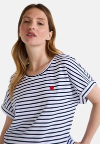 T-shirt à rayures à manches courtes en blanc et bleu marine avec un cœur brodé rouge sur la poitrine. Tissu en coton doux avec une coupe décontractée.