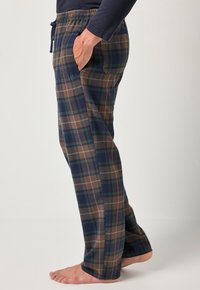 Los pantalones de lounge a cuadros presentan una combinación de colores marrón, marino y verde, con una cintura elástica y cordón ajustable, además de bolsillos laterales. Textura de tela suave.