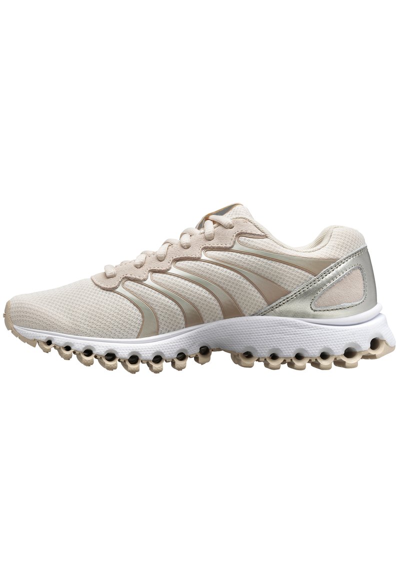 Zapatilla deportiva beige con parte superior de malla, acentos sintéticos y una suela texturizada con recortes circulares. Diseño ligero con cordones.
