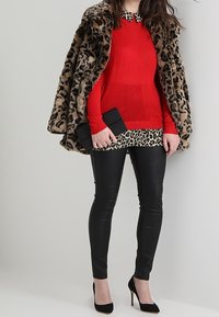 Manteau en fausse fourrure léopard, pull rouge, blouse à imprimé léopard, leggings en cuir noir, pochette noire et chaussures à talons hauts noires.