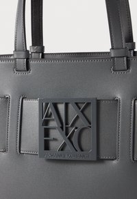 Borsa tote sintetica grigia con dettaglio logo in rilievo. Presenta doppi manici e una texture liscia con cuciture a contrasto.