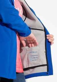 Veste bleue avec un extérieur lisse et un intérieur gris, dotée d'une poche étiquetée "HYDRA" et de symboles pour l'eau, le vent et la respirabilité.