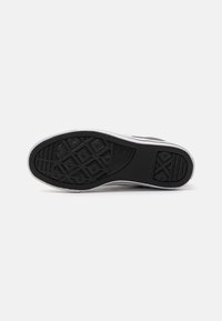 Black rubber sneaker sole with a textured surface, featuring triangular patterns and a white side stripe for added detail.