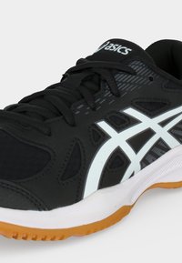 Αθλητικό παπούτσι Asics σε ασπρόμαυρο με μαύρα κορδόνια, λευκή μεσαία σόλα και καφέ λαστιχένια εξωτερική σόλα, με κλίση που δείχνει πλευρικές και δαχτυλικές λεπτομέρειες.