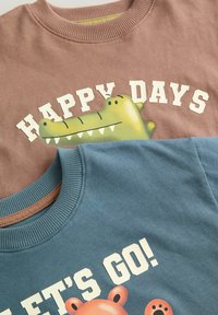 Dwie bawełniane bluzy: jedna brązowa z zieloną grafiką krokodyla i napisem "HAPPY DAYS", druga turkusowa z niedźwiedziem i napisem "LET'S GO!".