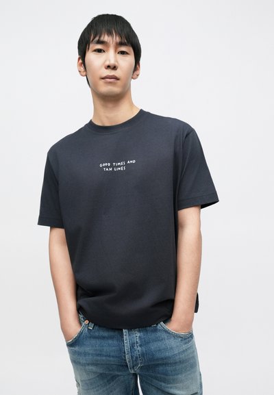 Μπλε ναυτικό βαμβακερό μπλουζάκι με κοντά μανίκια και στρογγυλή λαιμόκοψη, με λευκό κείμενο «GOOD TIMES AND TAN LINES» τυπωμένο στο στήθος.