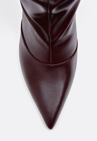 Bordová kožená vysoká čižma s špičatou špičkou, ktorá má hladký povrch a dizajn so záhybmi.
