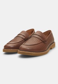 Mocasines de cuero marrón con un patrón tejido texturizado, acentos lisos y suela de goma. El diseño presenta una silueta elegante y costuras en contraste.