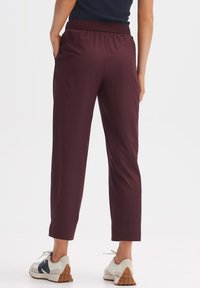 Bordeaux stretchbroeken met een elastische tailleband, twee achterzakken en een taps toelopende pijpen, gecombineerd met witte en grijze sneakers.