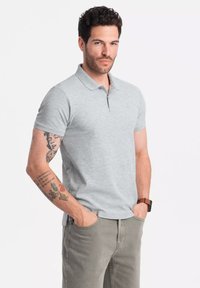 Polo de manga corta gris con cuello, hecho de una tela ligera, combinado con pantalones caqui claros. Cuenta con un pequeño logo en el pecho.