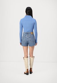 Pull bleu côtelé, short en denim taille haute avec ourlet effiloché, et bottes de cowboy crème avec des détails marron. Mettez l'accent sur la texture et la forme.