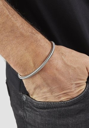 Silver metal bracelet on wrist, featuring a smooth, rounded design with a textured surface, worn over dark clothing.