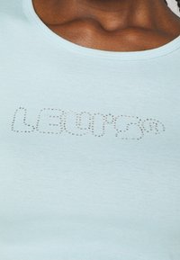 Top sans manches bleu clair avec une texture côtelée ornée de strass brillants formant le mot "Levi's" sur le devant.