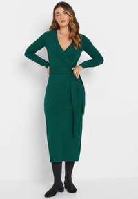 Grünes, langärmeliges Wickelkleid mit V-Ausschnitt, Taillengürtel und Knielänge. Weicher Stoff mit glatter Textur und figurbetonter Silhouette.