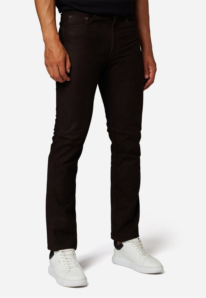 Bruine slim-fit jeans van zachte stof met zichtbare stiksels, gecombineerd met witte sneakers met zwarte accenten.