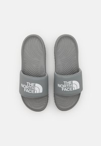 Grå sandaler med en strukturerad gummisula och ett brett band med en vit logotyp. Designen inkluderar vågmönster på sulan för bättre grepp.