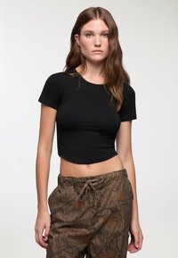 Maglietta nera corta con scollatura rotonda e maniche corte, abbinata a pantaloni marroni a fantasia con vita regolabile.