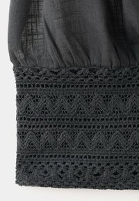 Gros plan d’un tissu foncé avec un haut froncé et des motifs horizontaux détaillés en dentelle et crochet sur le bord inférieur.