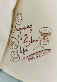 Krémová látka s hnědými liniemi nakreslenými ilustracemi konvice, zákusku a baguette, doplněná textem "Sní o pomalém životě."