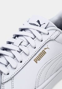 Bílá teniska Puma z kůže s bílými tkaničkami, zlatým logem Puma na boku a černým logem Puma na jazyku.