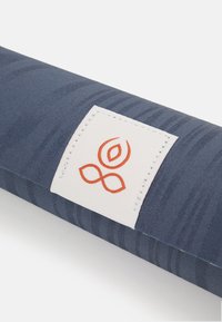 Sininen jooga-matto, jossa on teksturoitu kangas. Matossa valkoinen etiketti, jossa on oranssi logo ja ompelu. Maton pinnalla näkyy kuvioita.