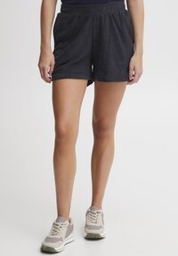Mørkegrå terry-klut shorts med elastisk liv. Stoffet har en myk tekstur. Kombinert med lysegrå og beige joggesko.