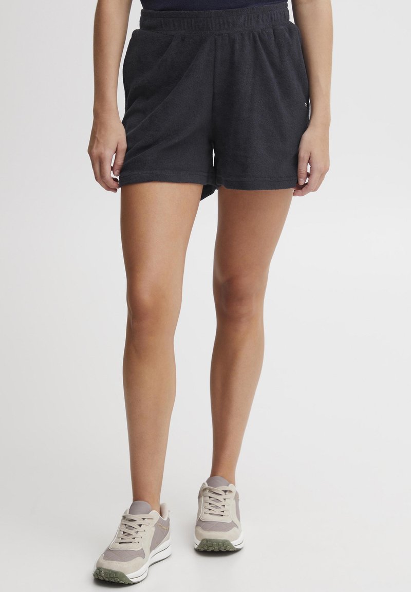 Mørkegrå terry-klut shorts med elastisk liv. Stoffet har en myk tekstur. Kombinert med lysegrå og beige joggesko.