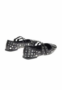 Scarpe flat nere con doppie fibbie, decorate con borchie e punte di varie dimensioni, presentate su uno sfondo bianco.