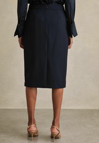 Tumši zila zīmulis svārki no gludas auduma ar paslēptu rāvējslēdzēju un pielāgotu piegriezumu. Valkāti ar ādas krāsas augstpapēžu sandales ar siksniņām.