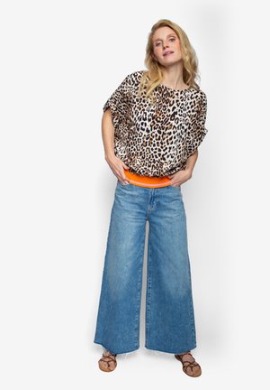 Bluse mit Leopardenmuster und lockeren Ärmeln, kombiniert mit blauem, hoch tailliertem, weitem Jeansstoff und einem orangen Taillenbund. Sandalen vervollständigen das Outfit.