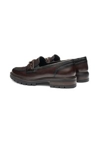 Een paar donkerbruine leren loafers met metalen bitdetail en dikke rubberen zolen, getoond vanaf de achterkant en de zijkant op een witte achtergrond.