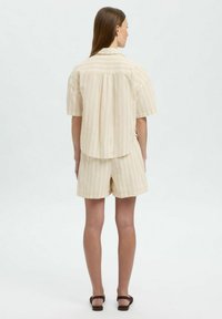 Kortærmet skjorte med krave og shorts sæt i lys gul med tynde striber. Stoffet ser let og blødt ud. Simpelt design.