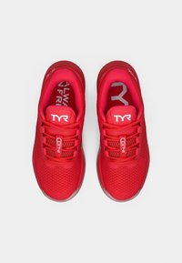 Baskets de sport rouges avec dessus en mesh, bout rond et semelle plate. Présentent un logo contrastant blanc et des lacets texturés pour un maintien sécurisé.