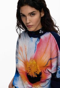 Hanorac cu imprimeu floral, având o floare mare și colorată în nuanțe de roz, portocaliu și galben, cu centru negru; confecționat din material moale, cu mâneci lungi.